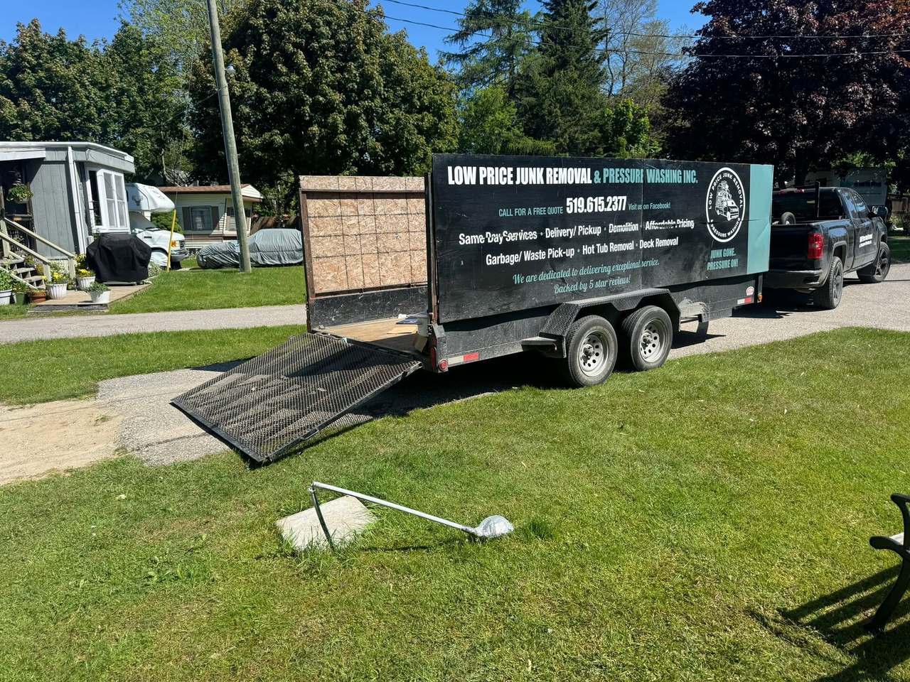 A front yard cleared of a large junk pile, with the branded LOW Price trailer loaded and ready to haul it away