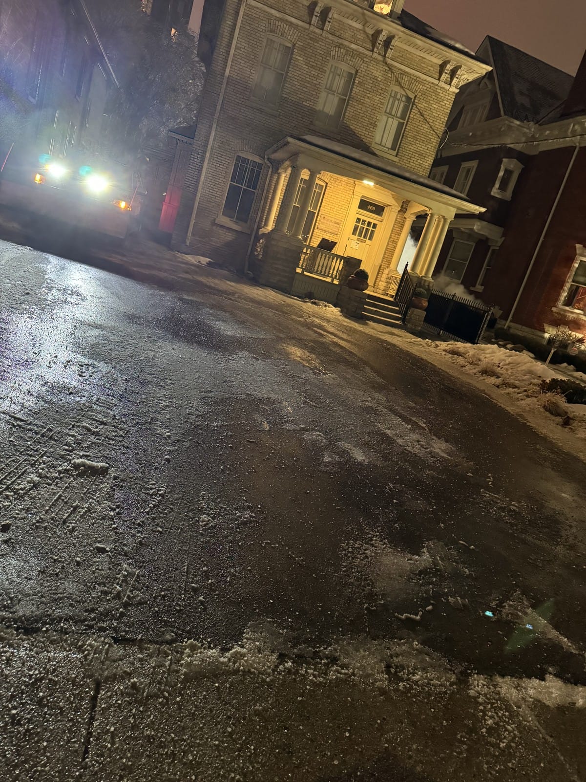 A property access road cleared and salted at night, with the plow truck's lights visible up the block
