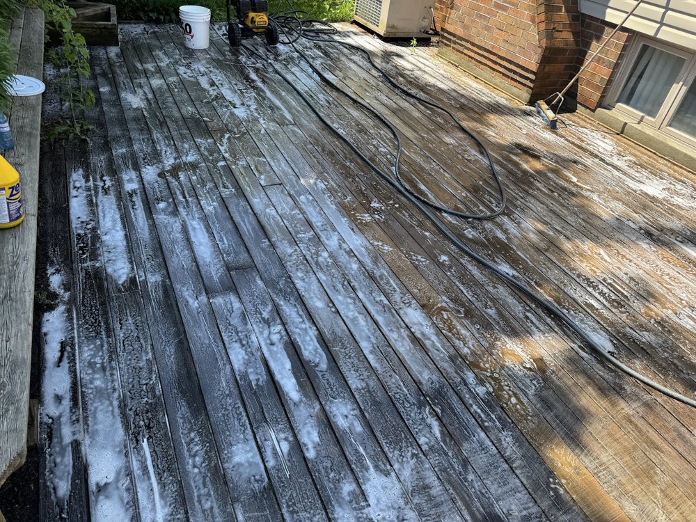 A weathered wood deck mid-wash, soap and dirt streaming off the boards under the pressure washer