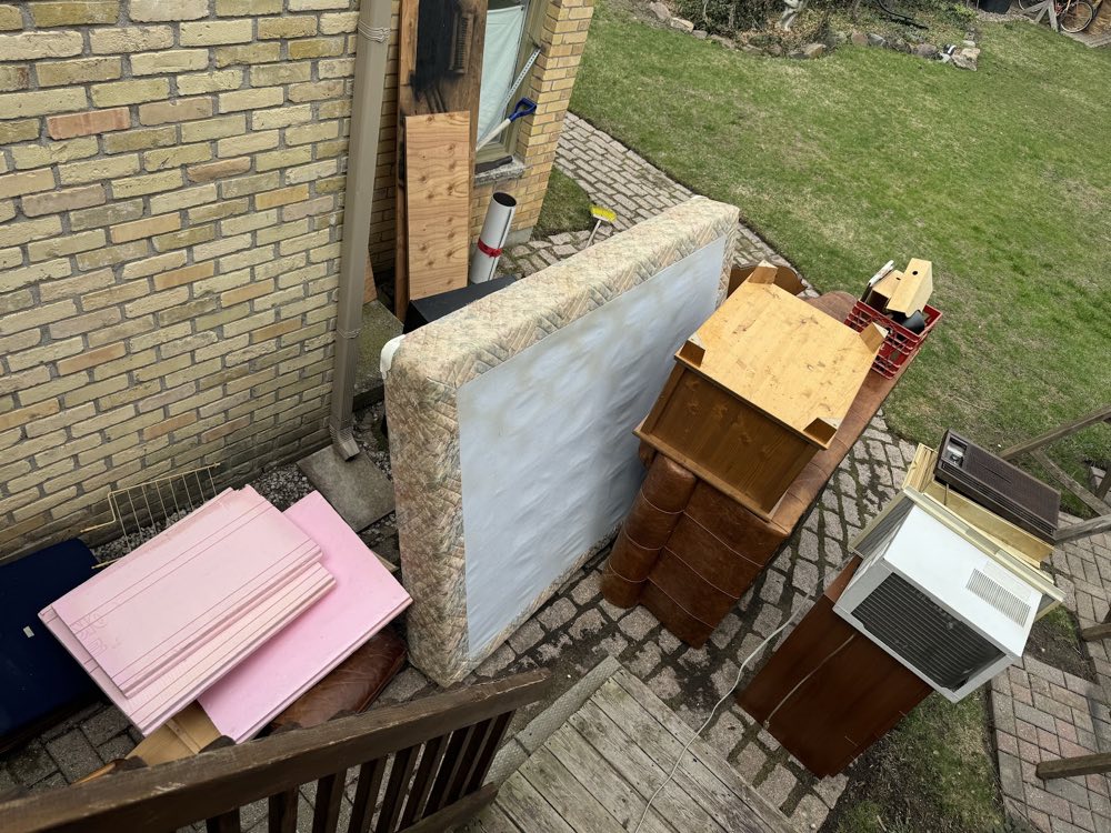 An old mattress, dresser, shelving and a window AC unit removed and stacked on a back patio for hauling